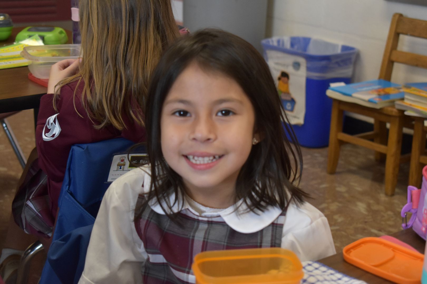 Smiling child seated at a classroom table.