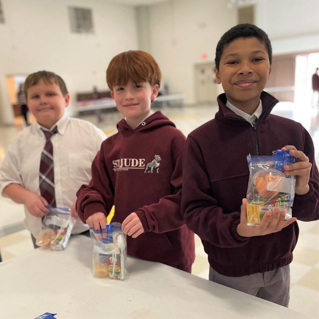Three children in school sweaters in a bright hallway.