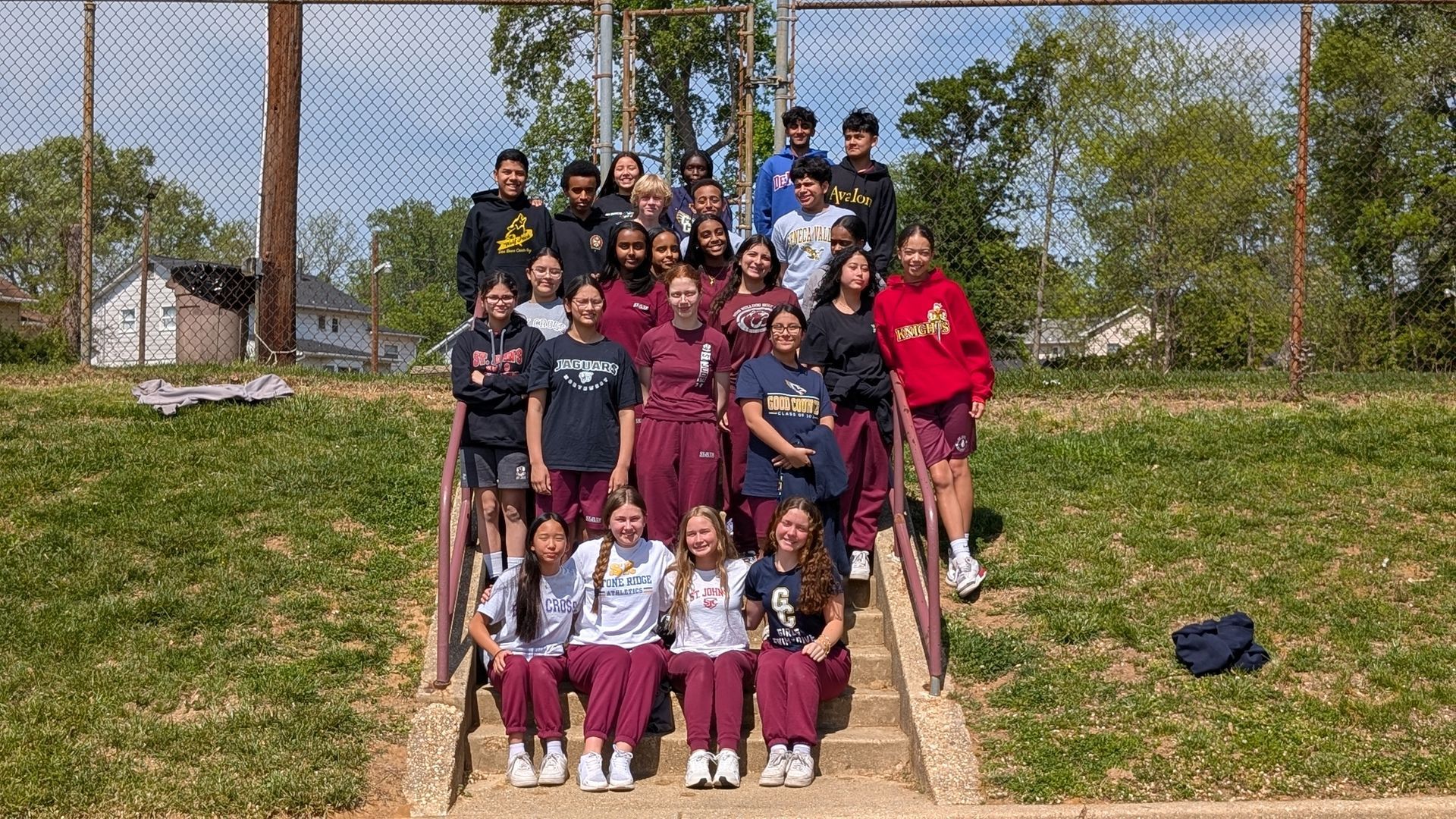 Large group posing on outdoor steps in front of a netted field on a sunny day