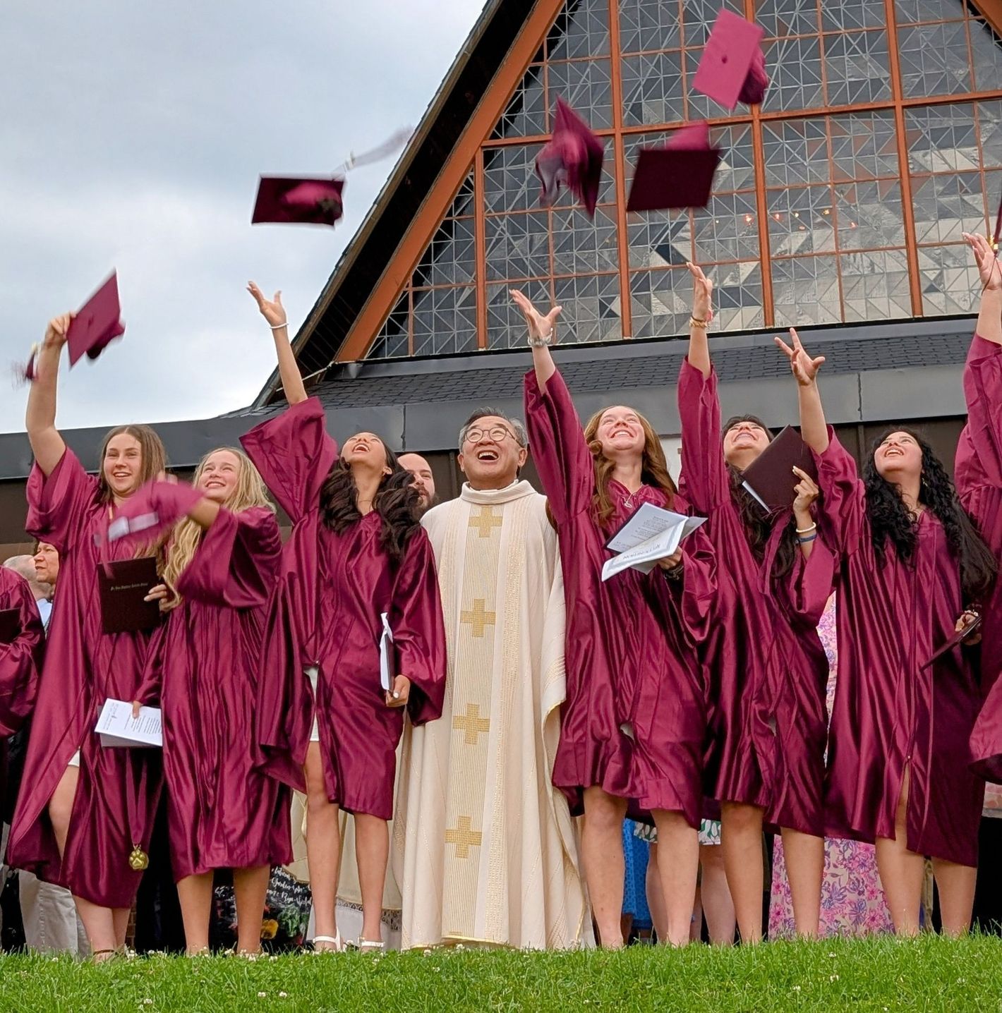Graduates in maroon caps and gowns toss caps in front of a church building
