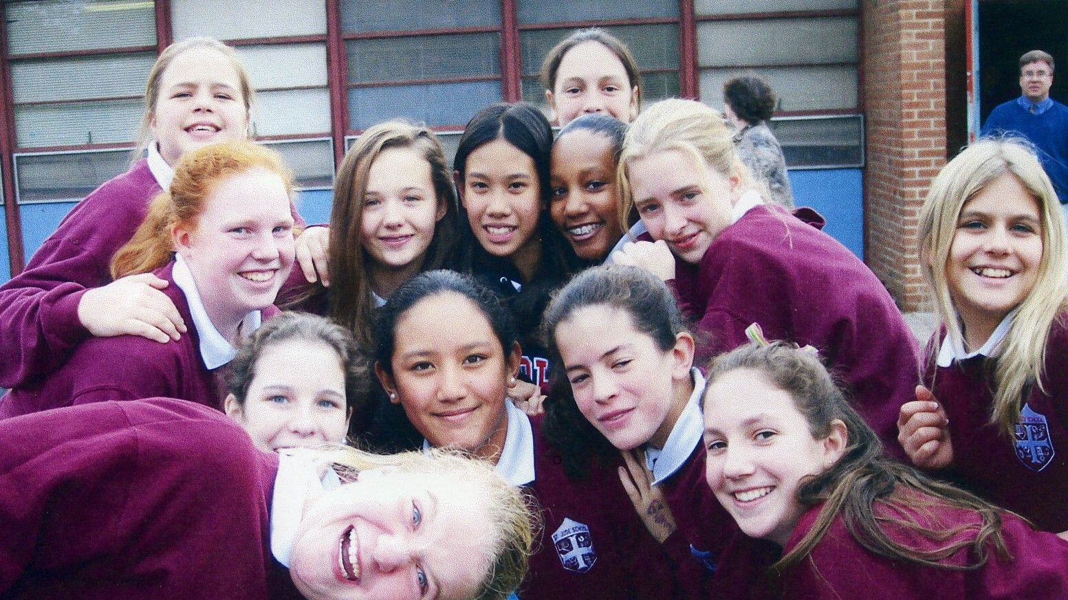 Group of smiling students in maroon sweaters posing closely together outdoors in front of a building