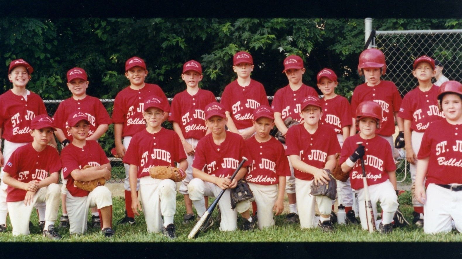 Youth baseball team in red jerseys and caps posing for a group photo on a field