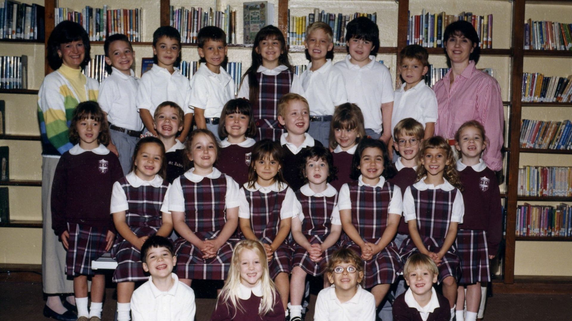 School class group portrait of children and adults standing and sitting on bleachers, many wearing uniforms.