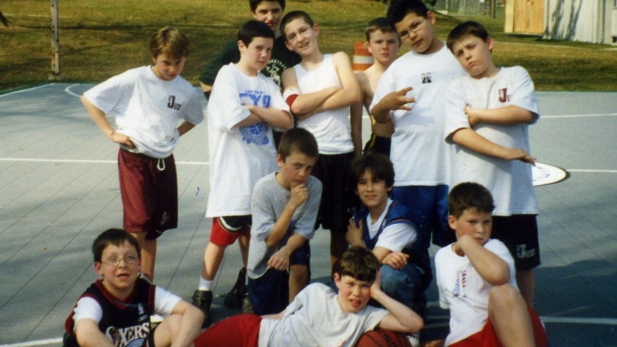 Group of boys posing together on an outdoor basketball court, smiling and making hand gestures