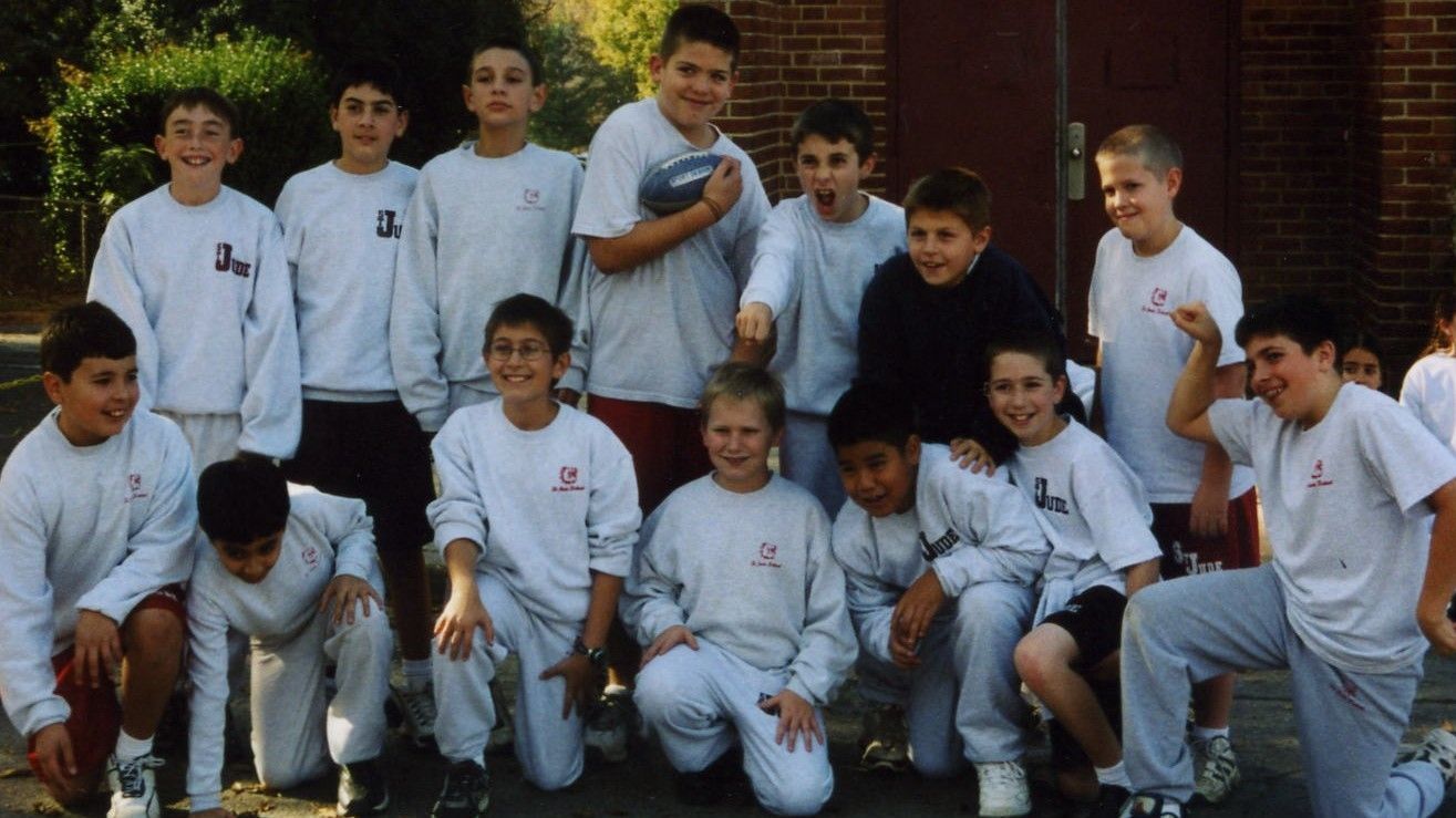 Group of children in white shirts posing outdoors in front of a brick building