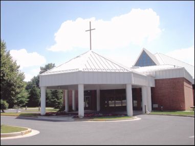 Church building with white peaked roof, cross, and brick walls under a blue sky