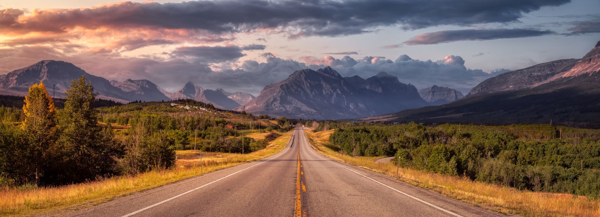 A long road stretches through a desert landscape toward distant mountains at sunset.