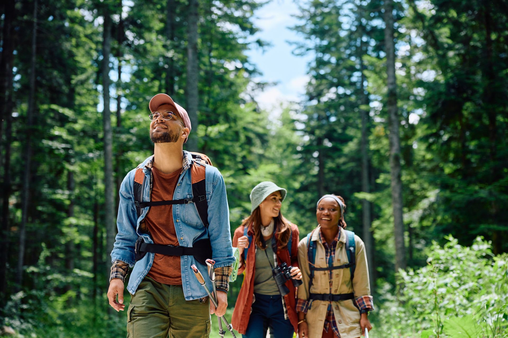 Three hikers with backpacks walking through a sunny forest trail