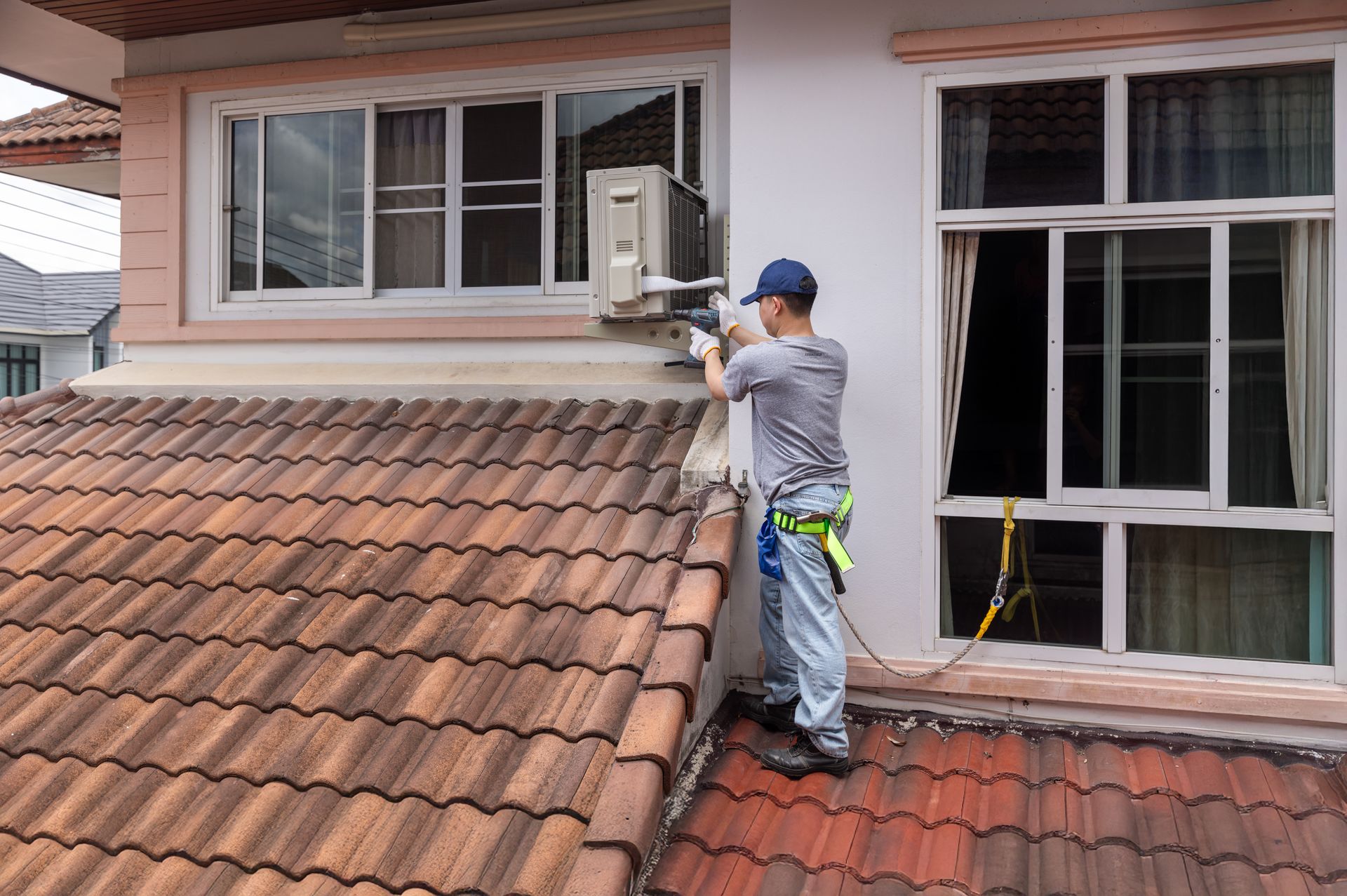 Technician installing or repairing a wall-mounted air conditioner unit beside a window on a tiled ro