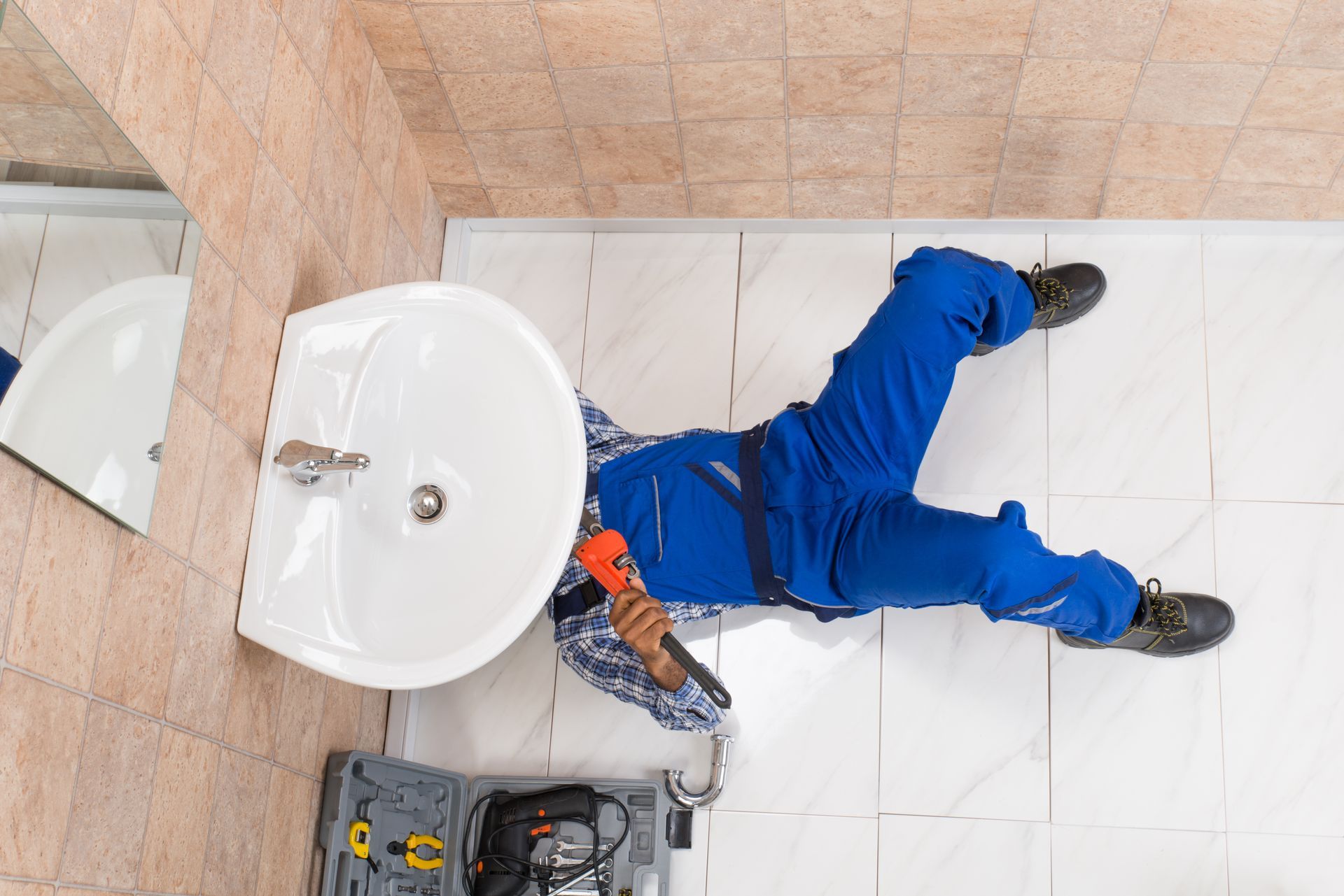 Plumber repairing bathroom sink with tools under vanity on hex tile floor during home plumbing job. Plumber repairing bathroom sink with tools under vanity on hex tile floor during home plumbing job.