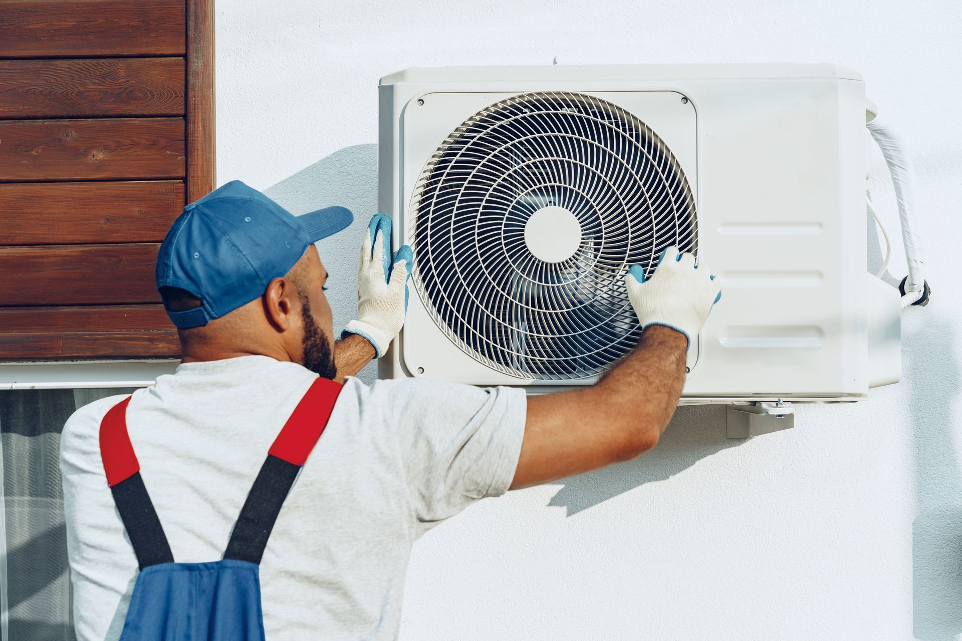 A technician in uniform carefully setting up an outdoor AC unit for proper cooling. A technician in uniform carefully setting up an outdoor AC unit for proper cooling.