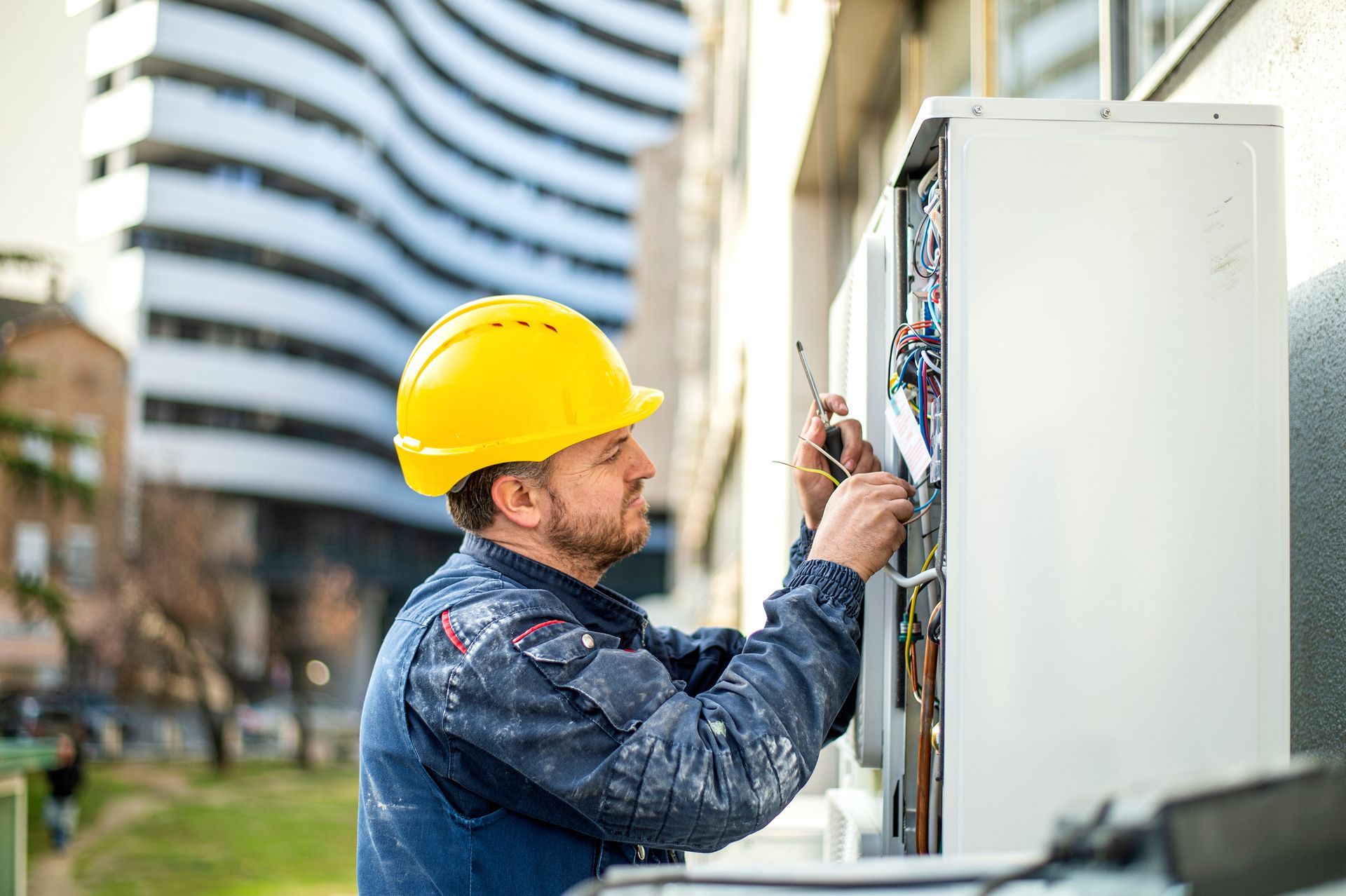 An air conditioner technician wearing a helmet services an outdoor commercial AC unit.