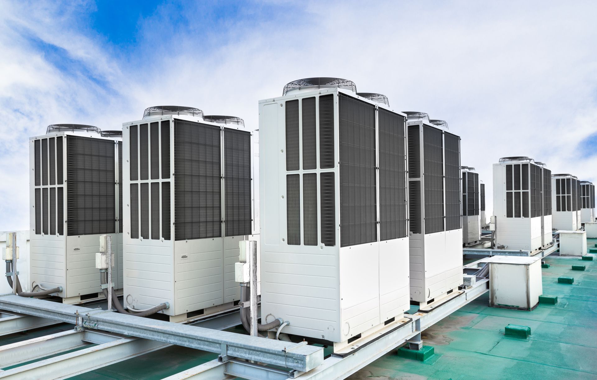 Rooftop AC units, white with black grilles, against a blue sky.