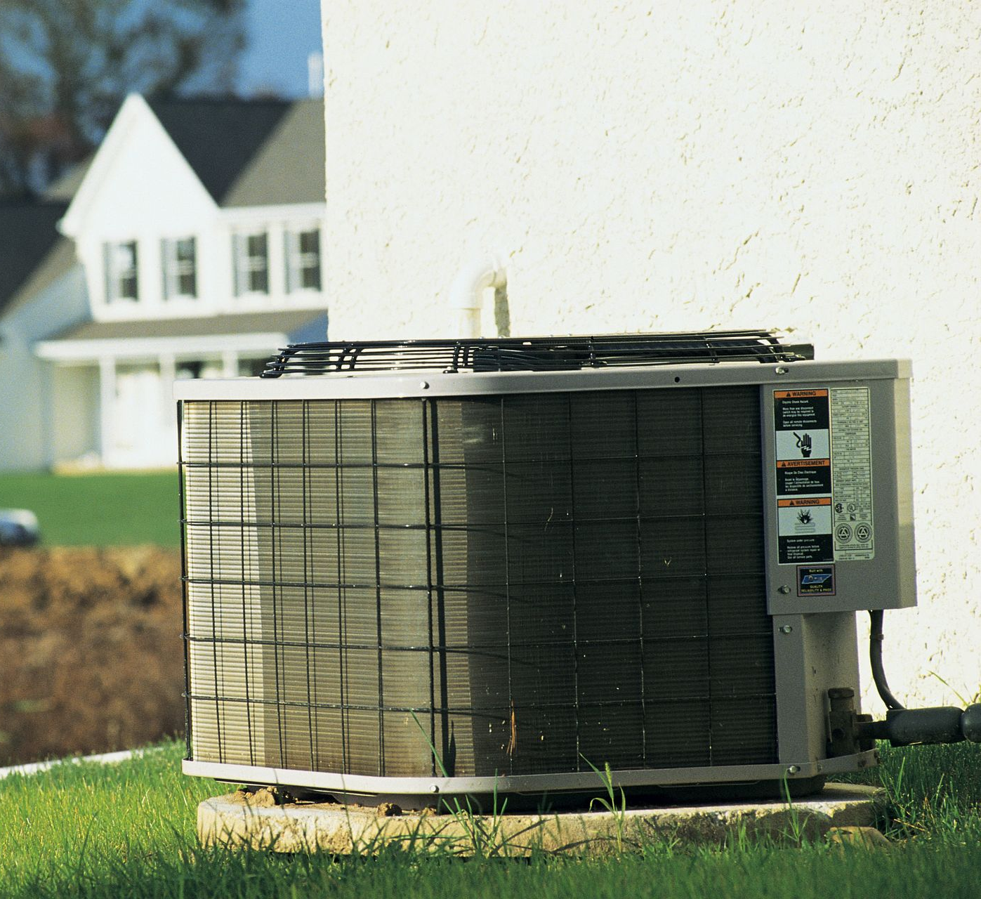 Air conditioning unit on a concrete pad near a white house with grass in front.