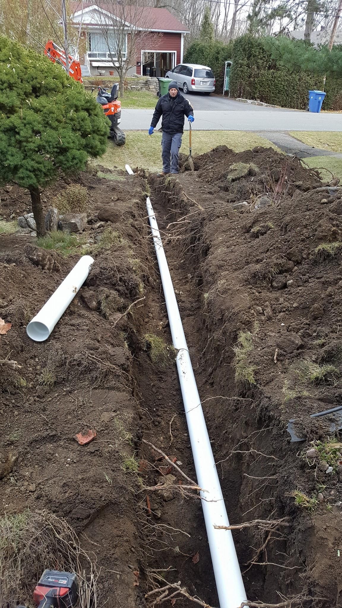 A man is standing in the dirt next to a large white pipe.