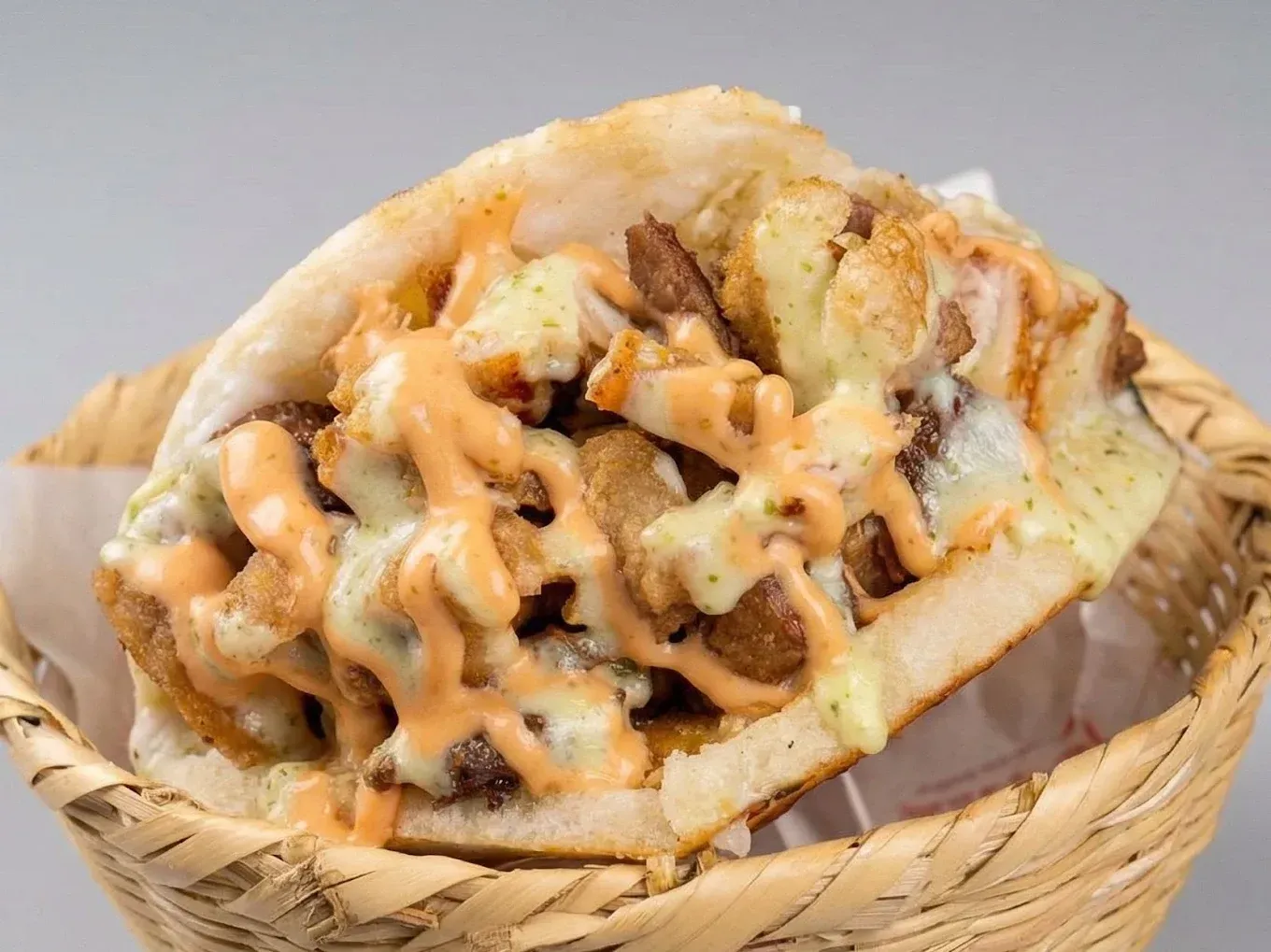 A basket of crispy fried snacks drizzled with sauce and toppings