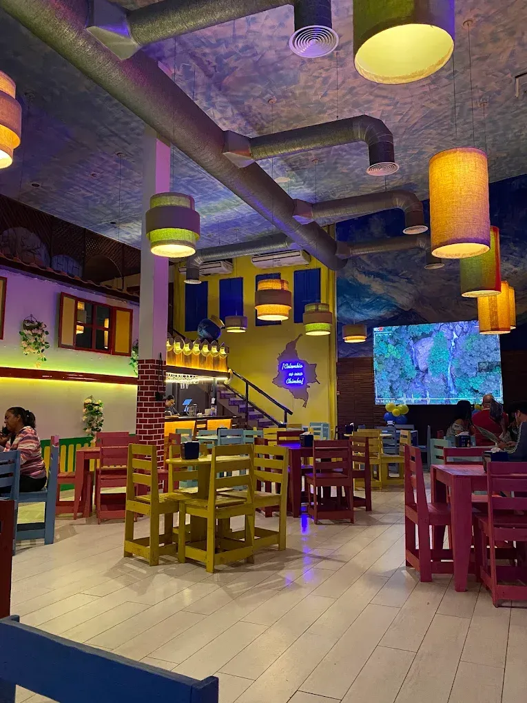 Colorful restaurant interior with wooden tables, hanging lights, and a large wall screen