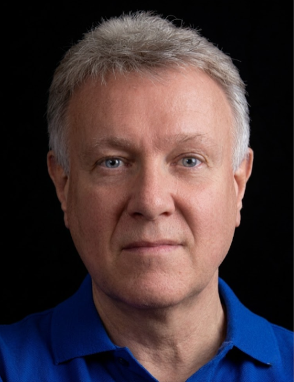 Portrait of a man with short gray hair wearing a blue collared shirt on a white background