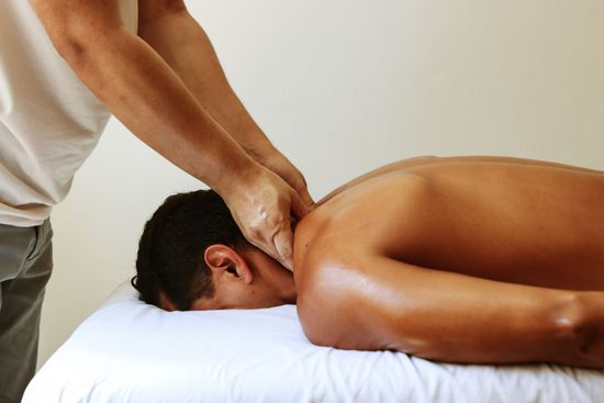 Person receiving a back massage on a white bed with sunlight through blinds