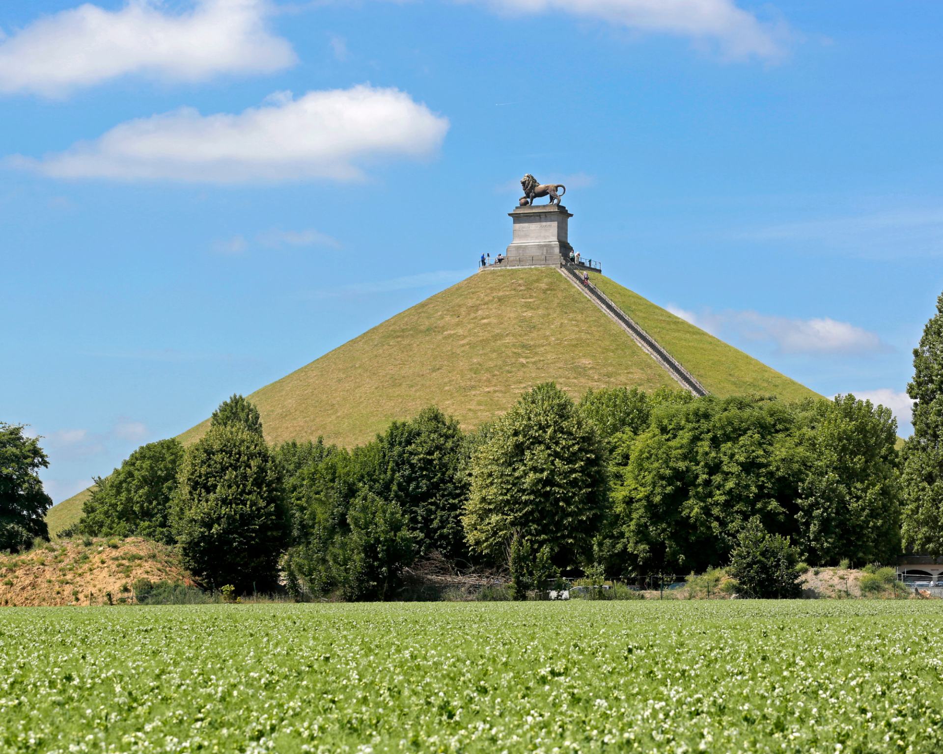 Colline pyramidale verdoyante surmontée d'un monument, se détachant sur un ciel bleu et dominant un champ herbeux.
