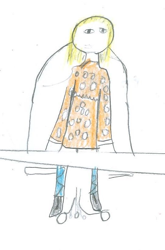 Person with blond pigtails wearing brown patterned coat, blue pants, and black boots, seated at a desk.