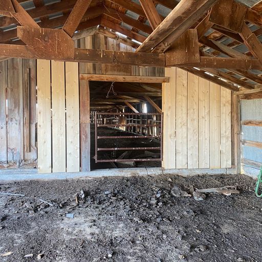 A barn with a ladder in the dirt in front of it