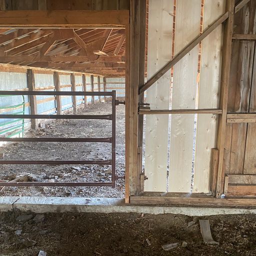 The inside of a wooden barn with a metal gate.