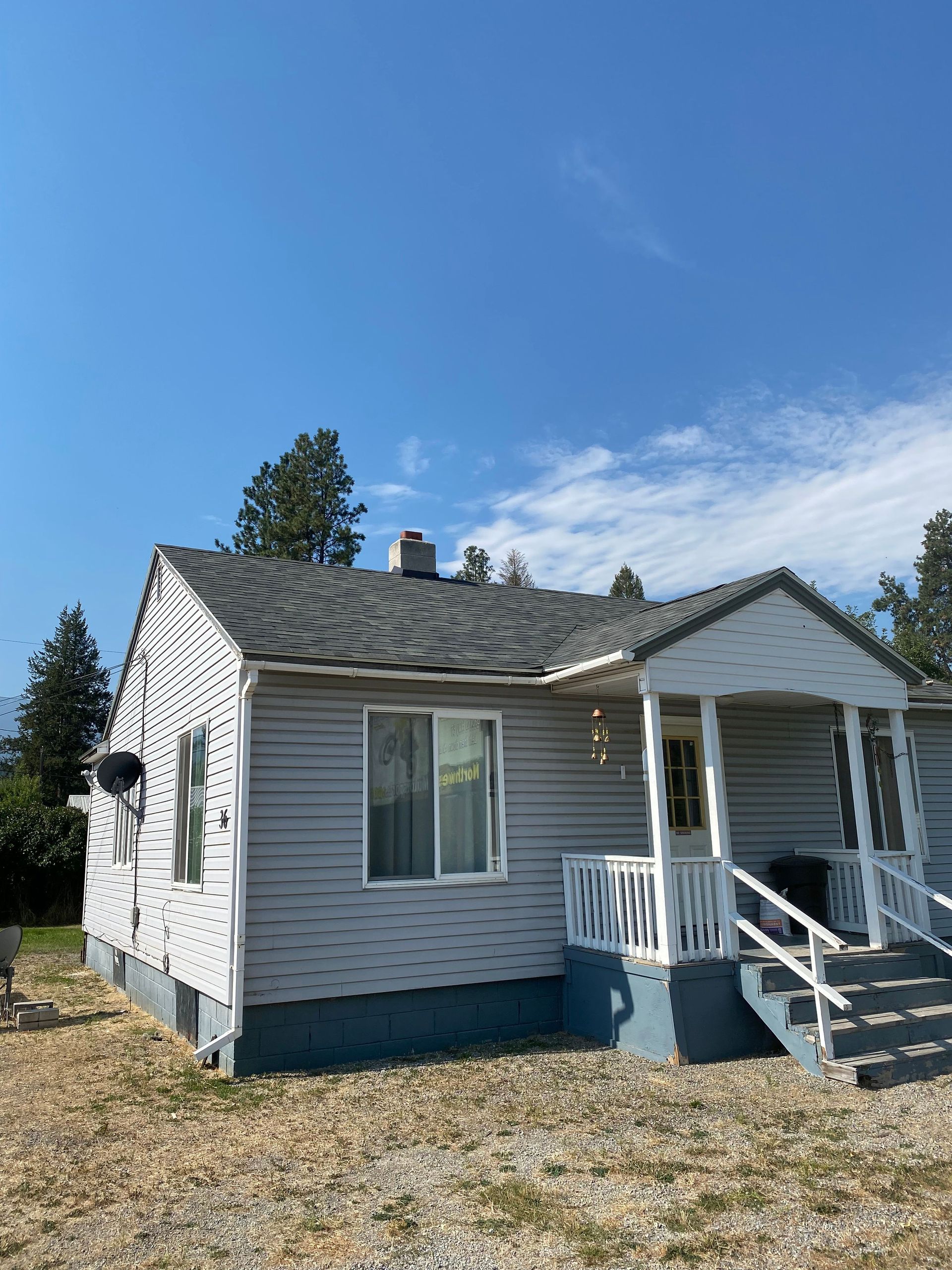 A small white house with a porch and stairs on a sunny day.