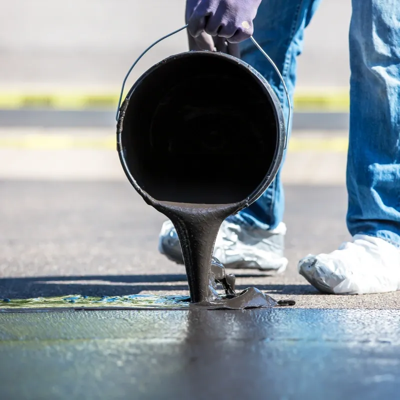 Road paving in progress; asphalt roller compacting freshly laid blacktop, worker in vest observing.