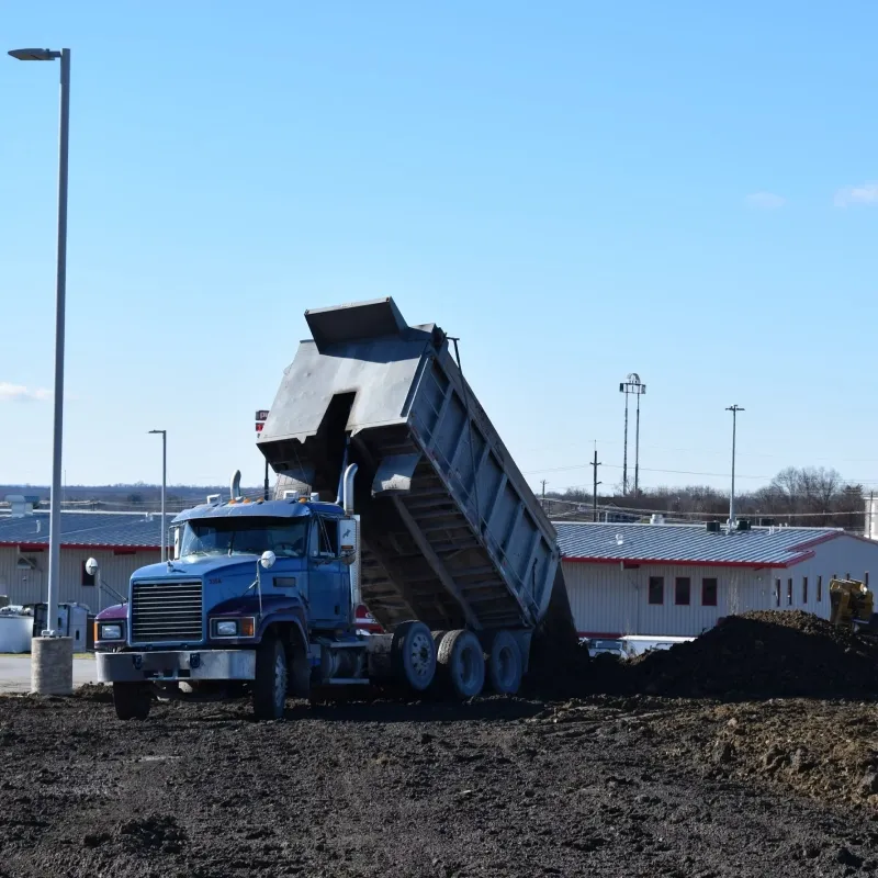 Road paving in progress; asphalt roller compacting freshly laid blacktop, worker in vest observing.