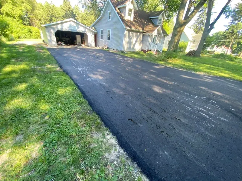 Freshly paved driveway leading to a white house with a garage in a sunny yard