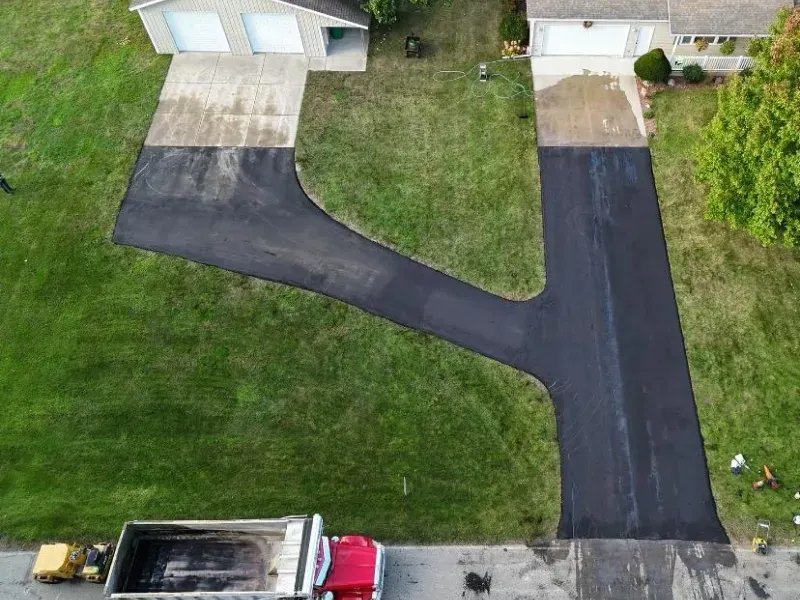 Aerial view of a newly paved black driveway leading to two garages beside a green lawn.