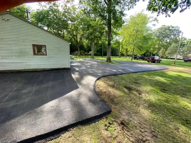 House with a paved driveway and grassy yard under trees, with a parked pickup truck nearby