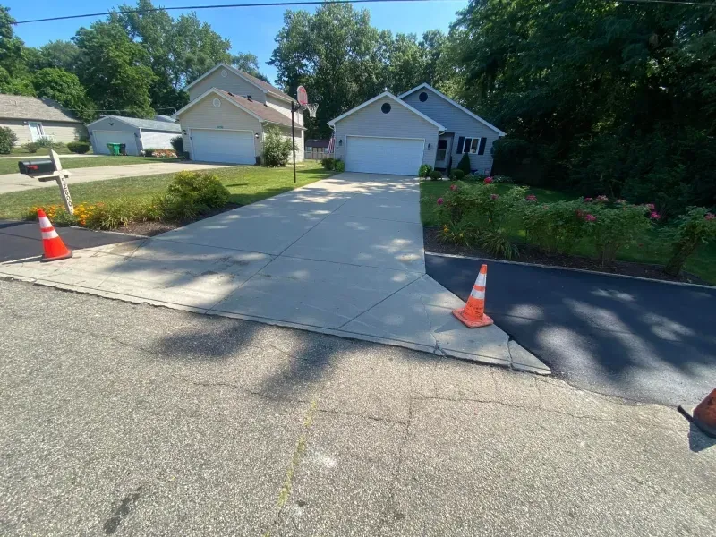 Freshly poured concrete driveway leading to a garage, marked by orange traffic cones in a suburban neighborhood