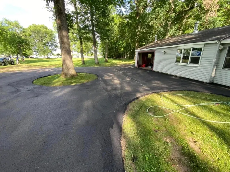 Curved asphalt driveway beside a white house and trees in a green yard