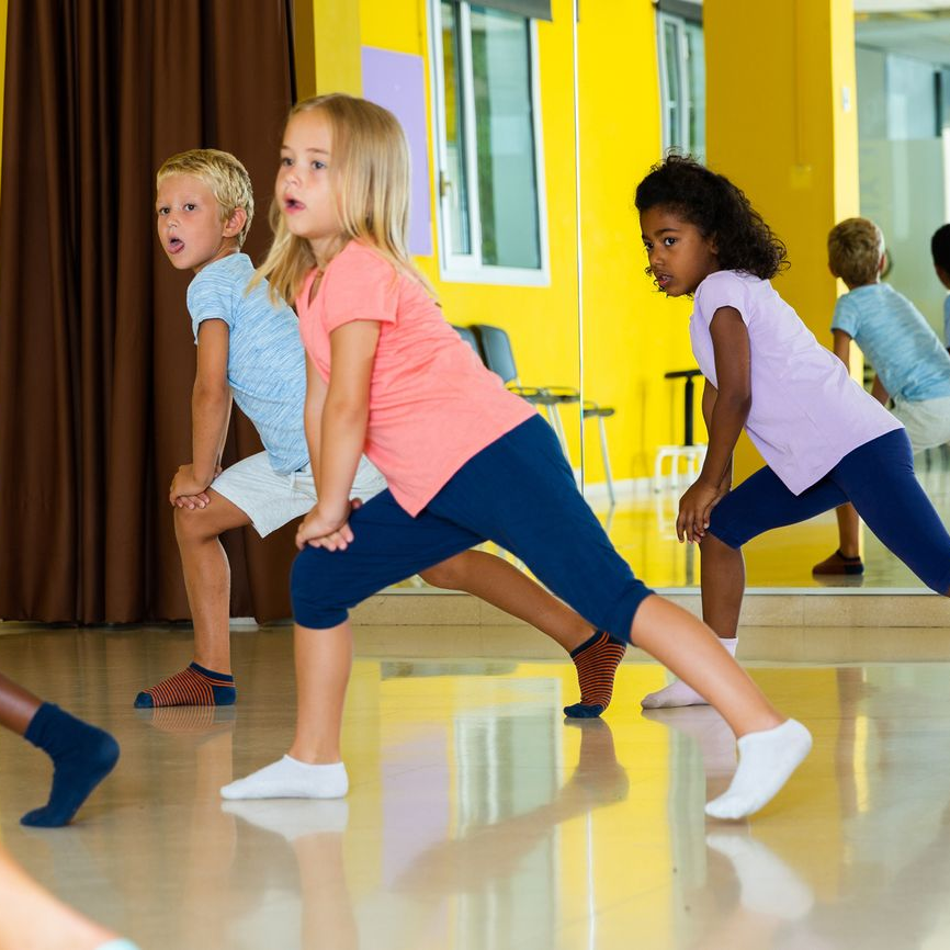 Children doing stretching exercises in a dance studio with yellow walls and a mirror. Children doing stretching exercises in a dance studio with yellow walls and a mirror.