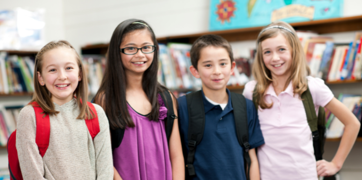 4th to 6th grade boys and girls in a classroom standing and smiling