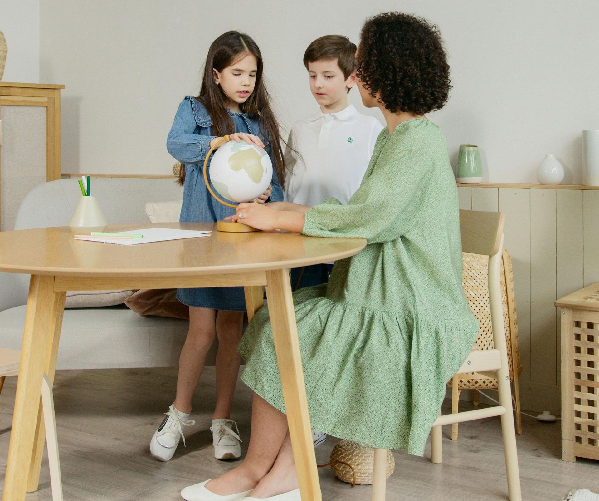 A mother or tutor, elementary school girl and boy, and a globe at a table at home