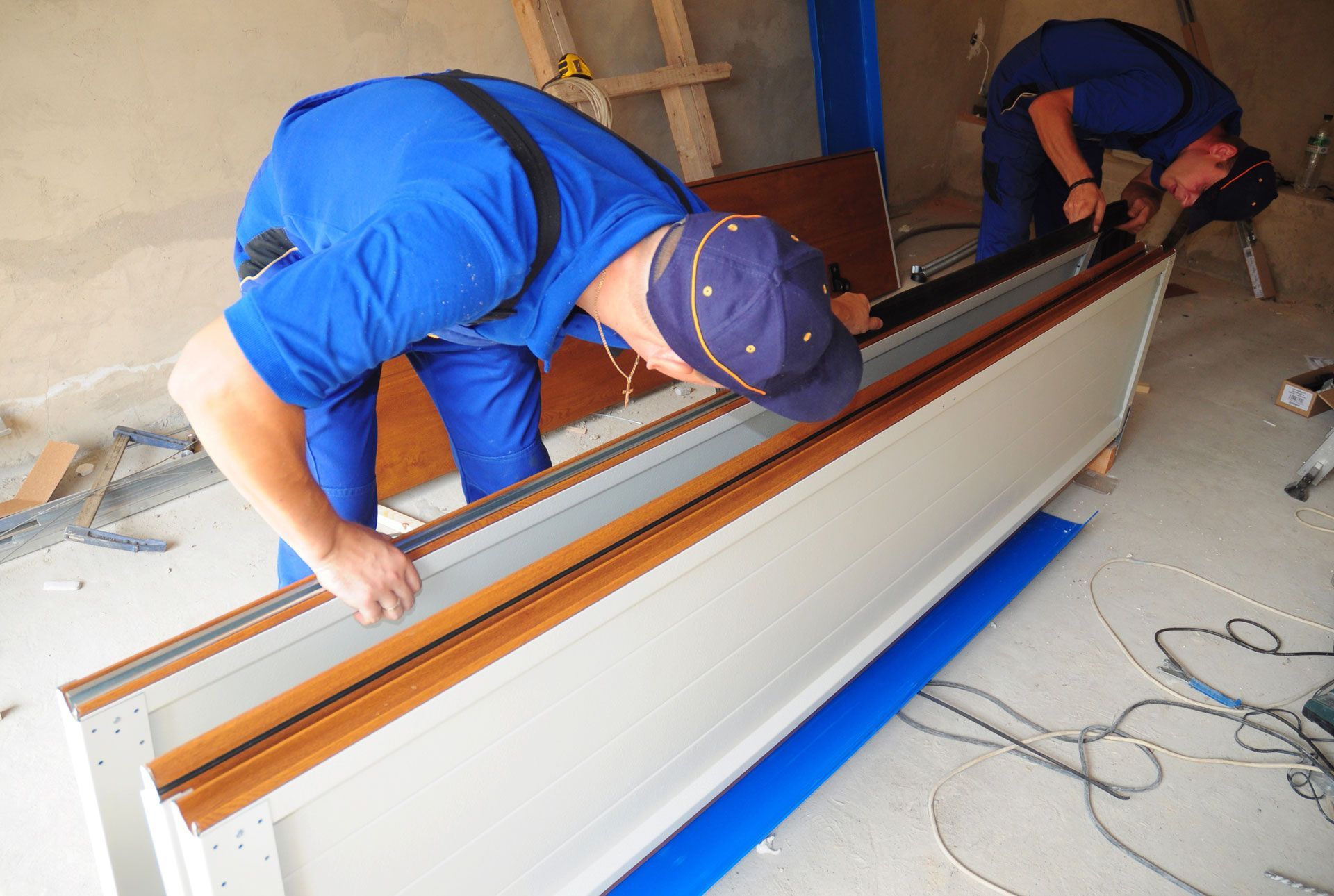 Two workers in blue coveralls installing a door frame.