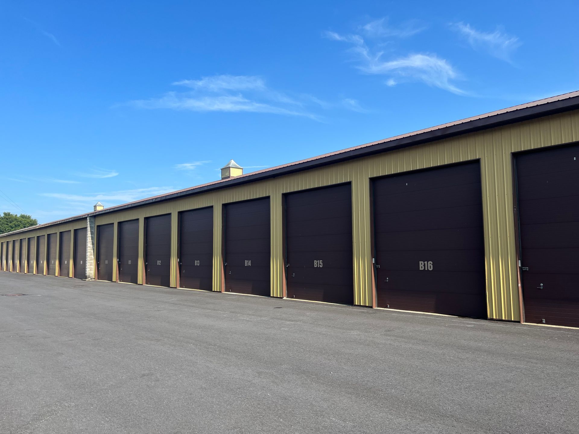 Row of brown storage unit doors with tan siding under a blue sky.