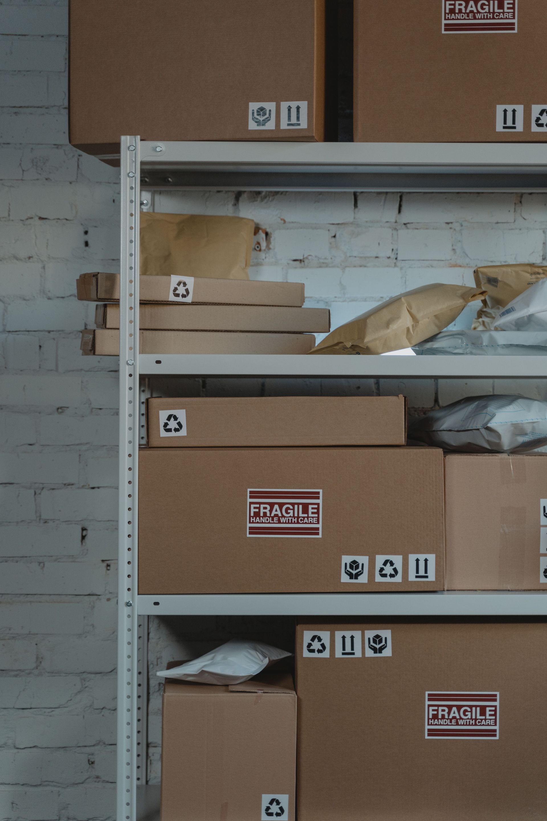 Shelves of cardboard boxes in a storage room against a white brick wall.