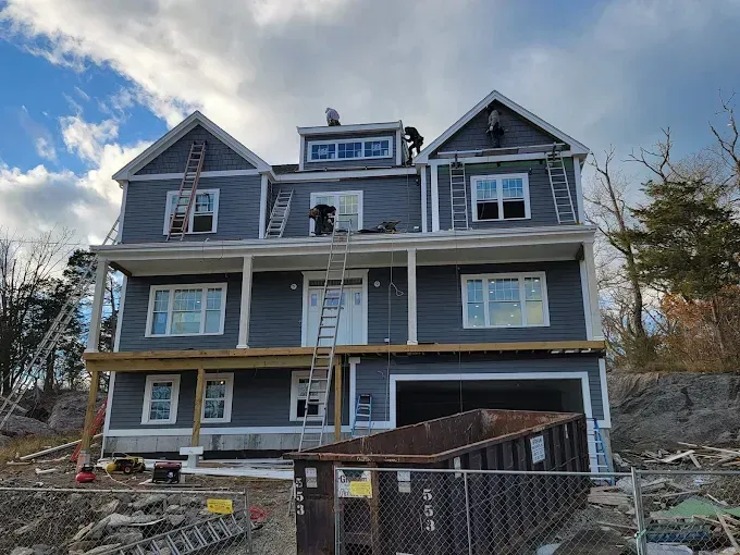 A large house is under construction with a dumpster in front of it.