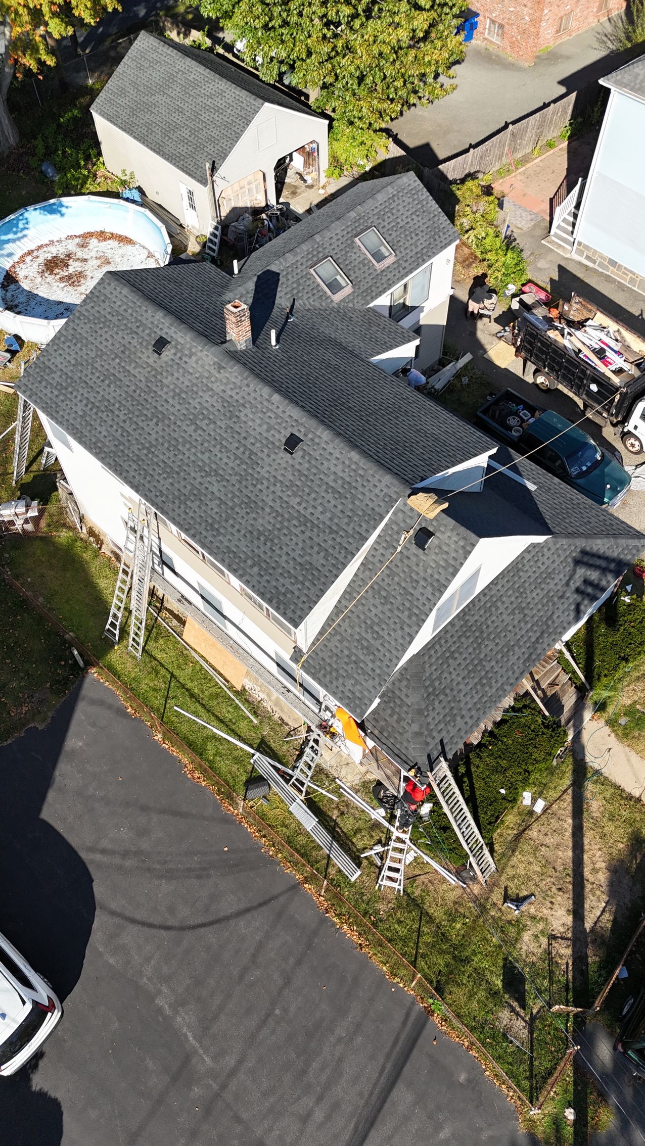 Aerial view of a house undergoing roof replacement with construction equipment, ladders, and materials visible.