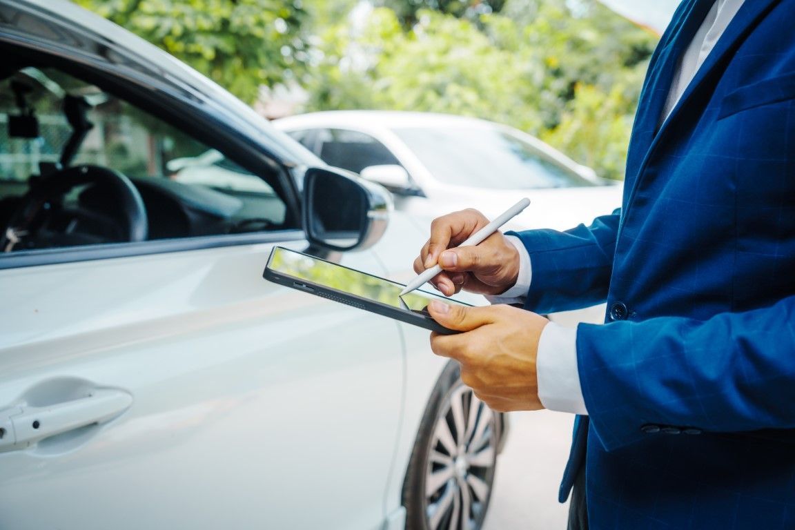 Person in blue jacket writing on a clipboard beside a white car