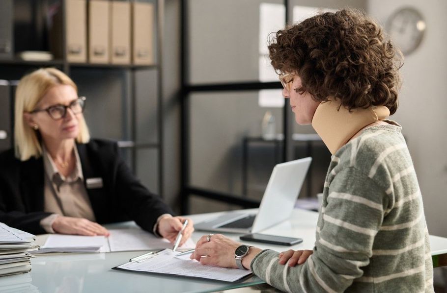 Two people in a meeting across a desk, reviewing papers with a laptop open nearby.