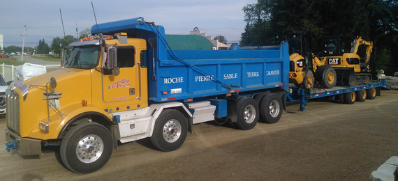 Un camion-benne jaune tire une excavatrice jaune sur une remorque.