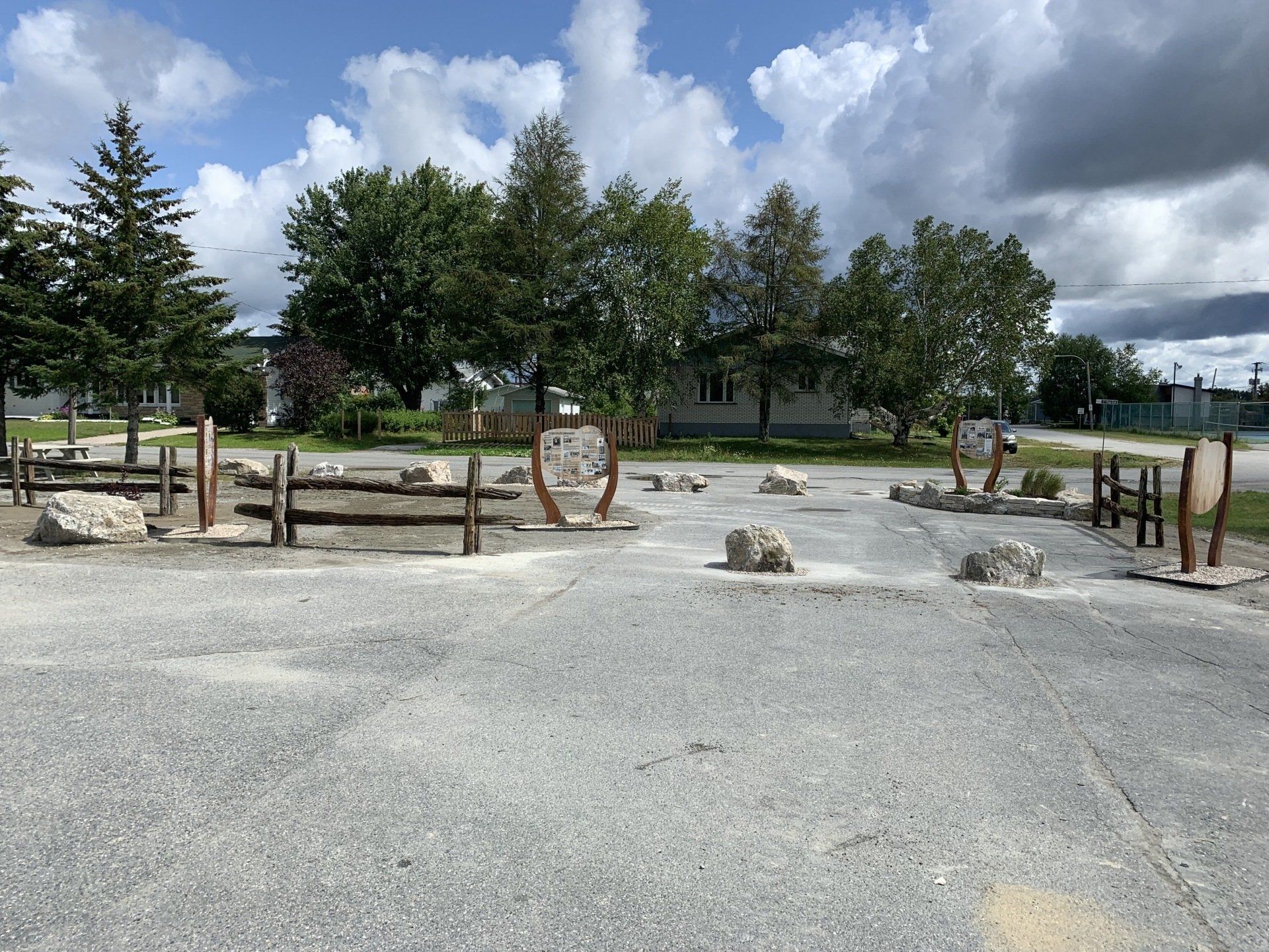 Allée de gravier bordant un parterre de jardin paillé agrémenté de pierres, de jeunes plants et de bouleaux. Forêt verdoyante en arrière-plan.