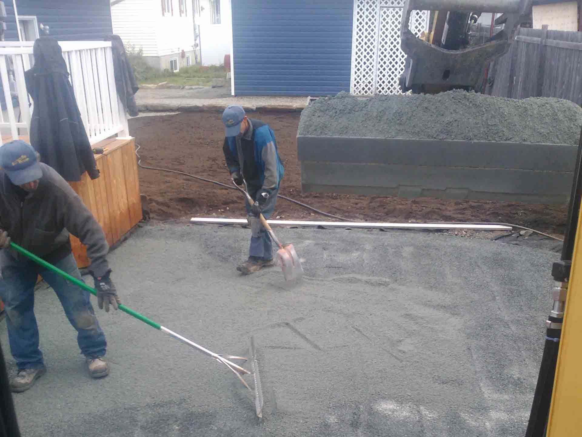 Deux hommes travaillent sur une allée en béton avec un râteau vert.