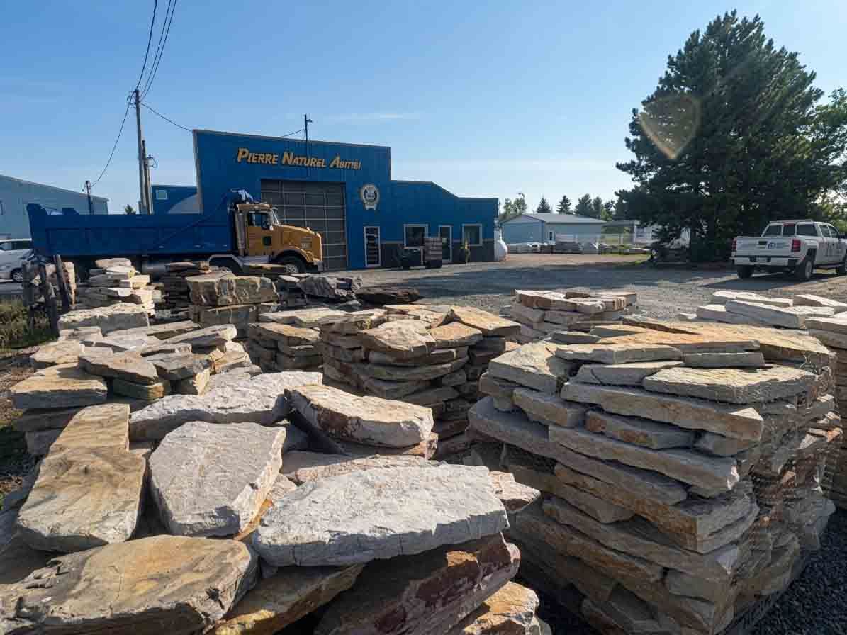 Des piles de dalles de pierre plates dans une cour devant un magasin de matériaux en pierre bleu, par une journée ensoleillée