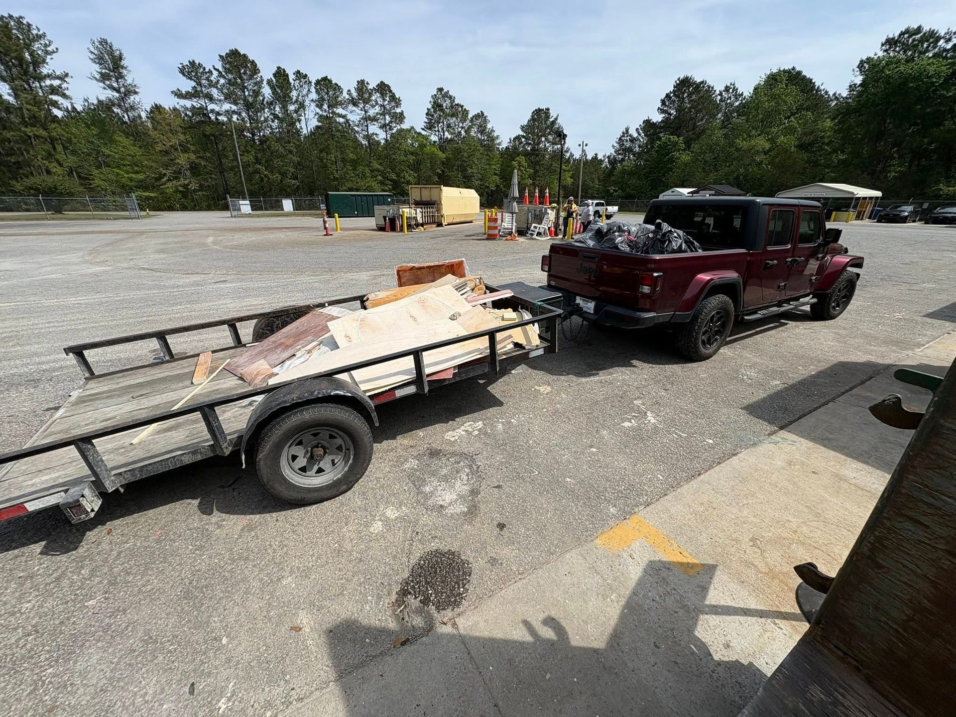 Maroon SUV towing a flatbed trailer with debris across a gravel lot under a clear sky